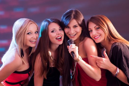 Four beautiful stylish girls singing karaoke at the club