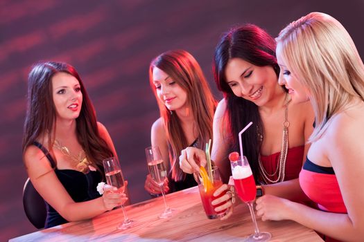 Female friends enjoying a night out sitting having cocktails at a table in a nightclub