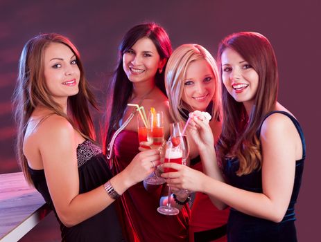 Group of four happy beautiful young female friends celebrating in a nightclub with glasses of cocktail in their hands