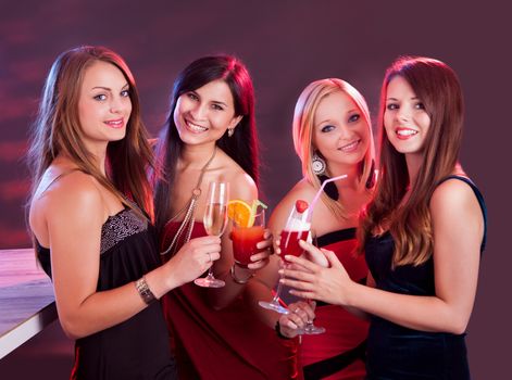 Group of four happy beautiful young female friends celebrating in a nightclub with glasses of cocktail in their hands