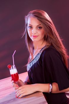 Glamorous beautiful woman in an evening dress holding a cocktail in her hand while standing at the bar in a nightclub
