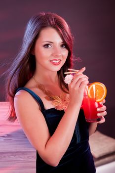 Glamorous beautiful woman in an evening dress holding a cocktail in her hand while standing at the bar in a nightclub