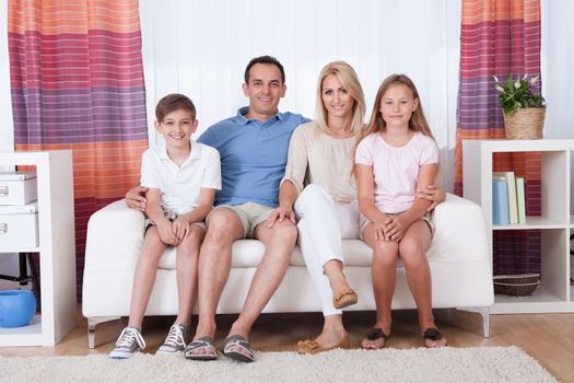 A Happy Family With Two Children Sitting On Sofa At Home