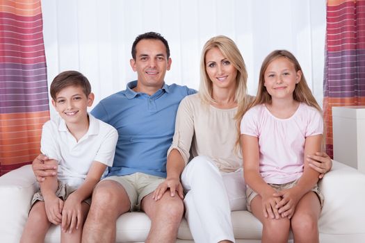 A Happy Family With Two Children Sitting On Sofa At Home