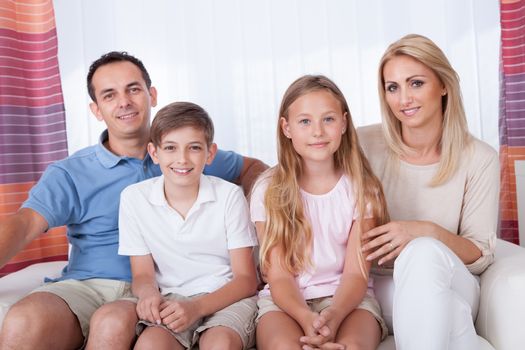 A Happy Family With Two Children Sitting On Sofa At Home