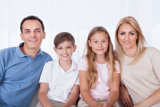 A Happy Family With Two Children Sitting On Sofa At Home