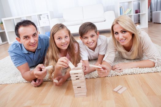 Happy Family Laying On Carpet Playing With The Wooden Blocks At Home