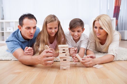 Happy Family Laying On Carpet Playing With The Wooden Blocks At Home