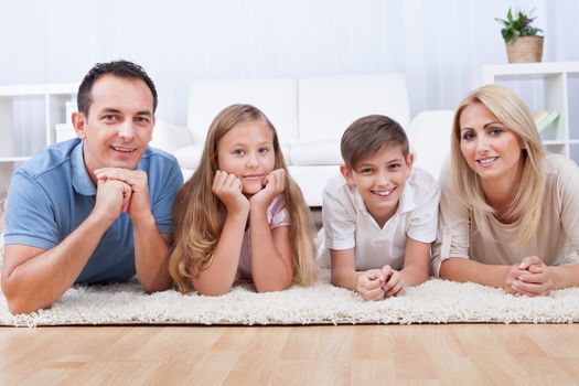 Portrait Of Happy Family With Two Children Laying On Carpet At Home