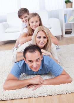 Happy Family With Two Children Lying Heaped On Carpet In Living Room At Home