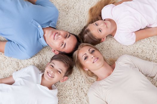 Close-up Of Happy Family Lying On Carpet Looking Up Heads Together At Home