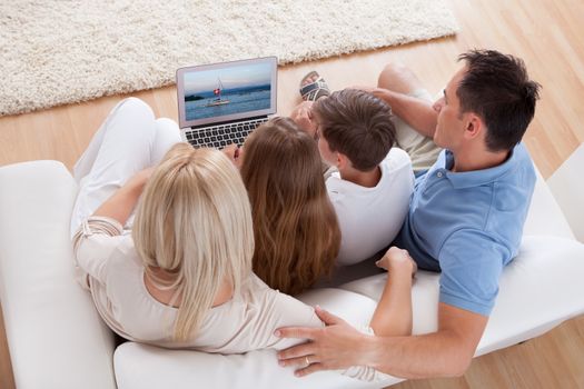 A Happy Family With Two Children Sitting On A Sofa Using Laptop At Home