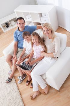 A Happy Family With Two Children Sitting On A Sofa Using Laptop At Home