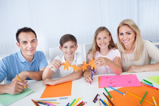 Portrait Of Happy Family Holding Paper People In Hand At Home