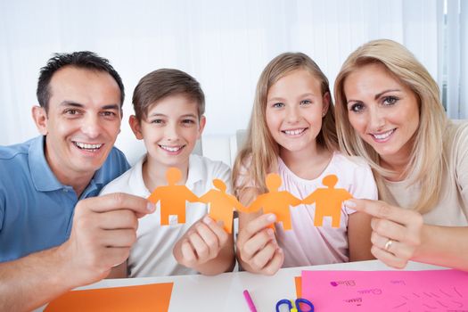 Portrait Of Happy Family Holding Paper People In Hand At Home