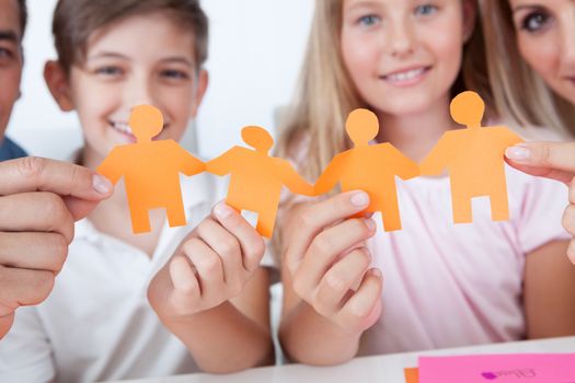 Portrait Of Happy Family Holding Paper People In Hand At Home