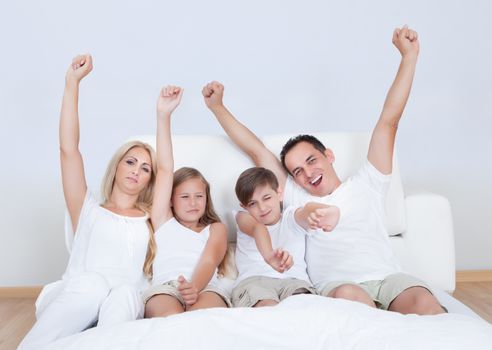 Portrait Of Happy Family With Two Children Sitting On Bed In Bedroom