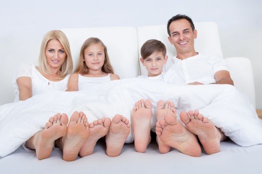 Happy Family With Two Children In Bed Under Cover Showing Feet, Indoors