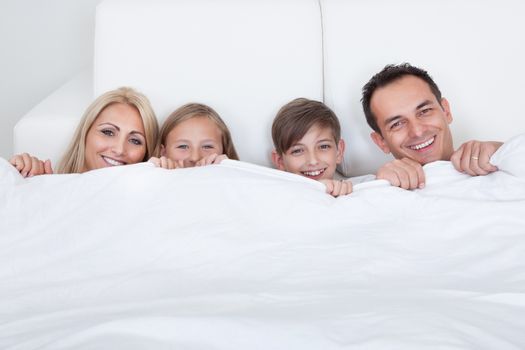 Happy Family With Two Children In Bed Under Cover, Indoors