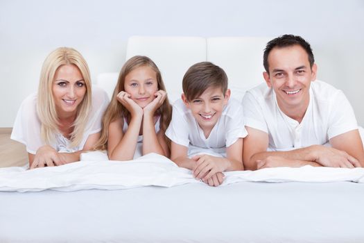 Happy Family With Two Children Lying On Bed At Home