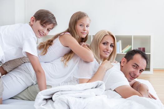 Happy Family With Two Children Lying Heaped On Bed At Home