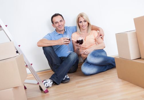 Couple Sitting Between Cardboard Boxes And  Holding Wine Glass, Indoors