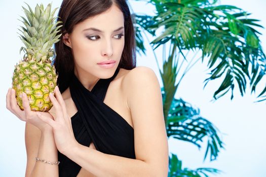 Woman holding pineapple in front of a palm tree