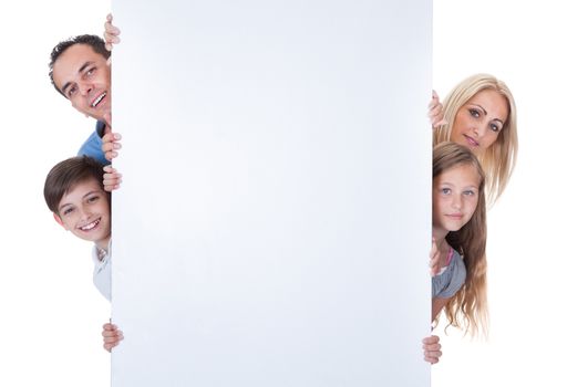 Portrait Of Family With Two Children Peeping Behind Blank Board On White Background