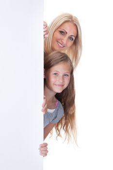 Portrait Of Mother and Girl Peeping Behind Blank Board On White Background