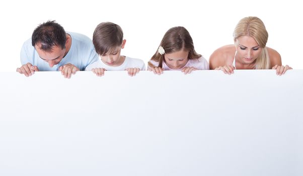 Portrait Of Family With Two Children Behind Blank Board On White Background