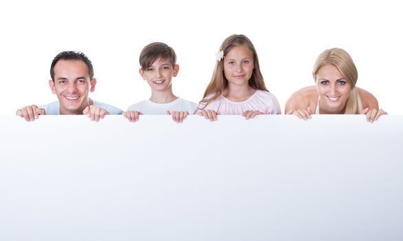 Portrait Of Family With Two Children Behind Blank Board On White Background