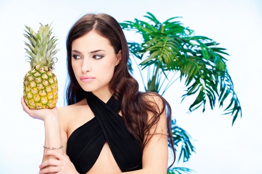 Pretty dark hair woman holding pineapple in front of a palm tree