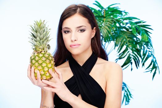 Pretty woman holding pineapple in front of a palm tree