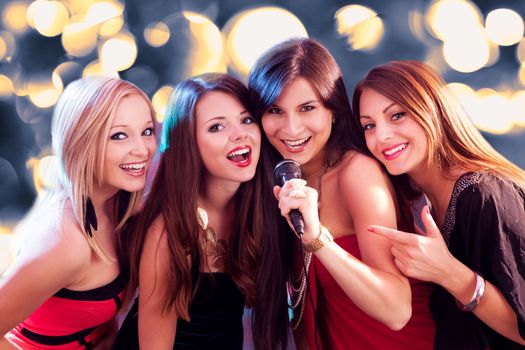 Four beautiful stylish girls singing karaoke at the club