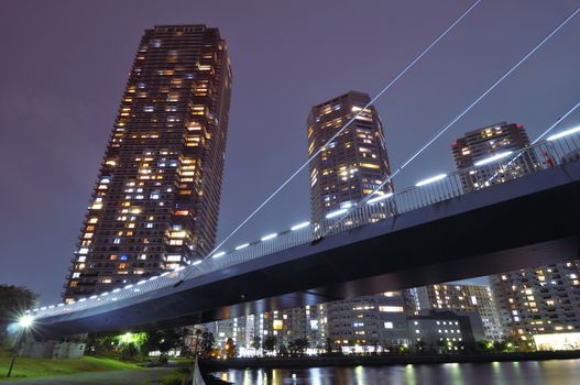 huge residential skyscrapers with illuminated windows beyond illuminated suspension bridge structure in Tokyo, Japan