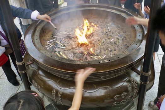 Buddhist smoking urn with burning incense sticks with many people around it