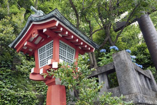 traditional Japanese wooden lantern in green forest with stone gate fragment behind