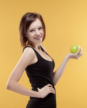 teenage girl holding a green apple smiling - isolated on yellow