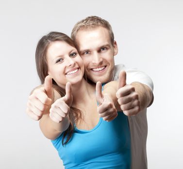 young couple showing both thumbs up smiling- isolated on gray