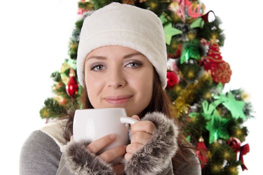 Woman in fur hat and mittens with mug under Christmas tree