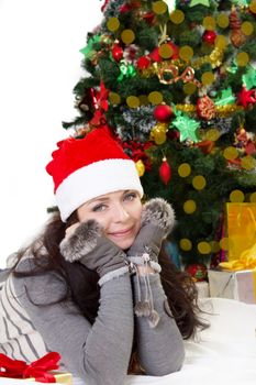 Smiling woman in Santa hat and fur mittens lying under Christmas tree