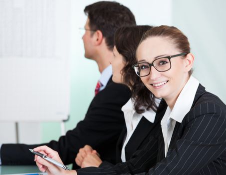 Smiling successful businesswoman wearing glasses looking at the camera while seated in a meeting with her colleagues