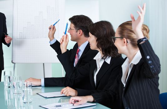 Manager or senior business executive standing in front of a graph giving a presentation to staff or colleagues seated at a table