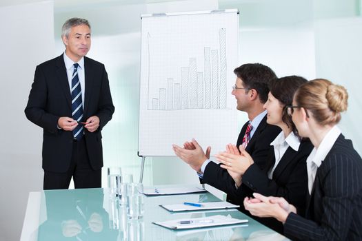 Diverse business colleagues seated around a table clapping after a staff presentation by a manager or senior executive