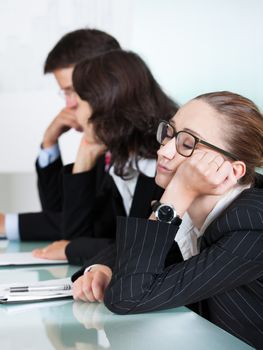 Bored businesswoman sleeping in a meeting as her colleague who is giving the presentation talks in the background