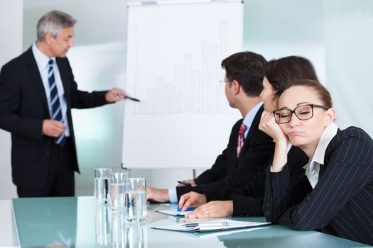 Bored businesswoman sleeping in a meeting as her colleague who is giving the presentation talks in the background