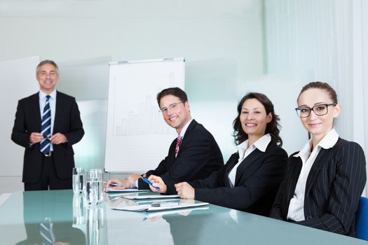Smiling successful business team holding a meeting sitting around a white glass topped table with one executive