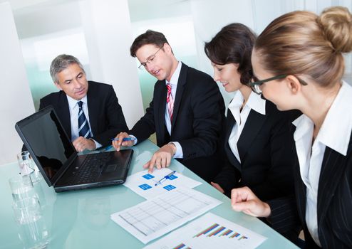 Group of diverse business executives holding a meeting around a table discussing graphs showing statistical analysis