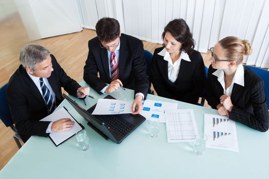 Overhead view of a group of diverse business executives holding a meeting around a table discussing graphs showing statistical analysis
