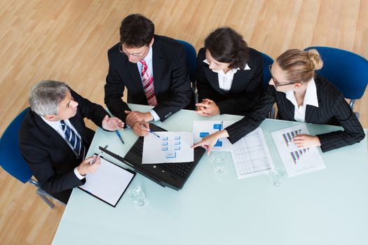 Overhead view of a group of diverse business executives holding a meeting around a table discussing graphs showing statistical analysis